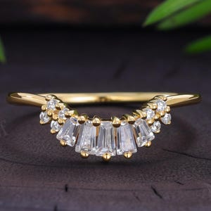 Peut inclure: Une bague incurvée en or ornée d'une rangée de pierres transparentes taille baguette au centre, flanquée de pierres plus petites taille ronde de chaque côté, fixées par des griffes suivant la courbe de l'anneau.