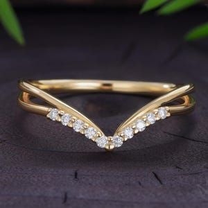 Peut inclure: Une bague en forme de V en or avec un anneau délicat présentant un design divisé sur le dessus. La pointe centrale du chevron est ornée d'une rangée de petites pierres claires taillées en rond, serties sur la surface avant de l'anneau en or poli.