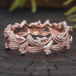Peut inclure: Une bague en or rose présentant un motif continu de feuilles ou de vignes sculptées qui fait le tour de la circonférence. De petites pierres rondes et transparentes sont serties à intervalles dans le design végétal en métal.