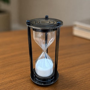 May include: An hourglass featuring a dark metallic frame with a circular top and base, connected by four vertical pillars. The central glass bulb contains white sand, with the majority of the sand collected in the bottom chamber of the device.