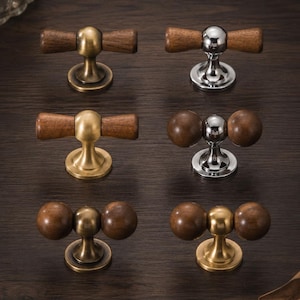 May include: A collection of six cabinet knobs featuring a combination of dark brown wood and metal bases. The set includes three knobs with cylindrical wooden handles and three with spherical wooden handles, finished in brass, chrome, and bronze tones.
