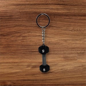 May include: A black dumbbell keychain with a silver chain and a silver ring. The dumbbell has the numbers 5 and 9 on each end.