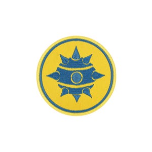 Pode incluir: Um emblema bordado circular com um fundo amarelo brilhante e uma borda azul. No centro, um gráfico azul em forma de maça pontiaguda é representado com um elemento circular no meio e vários espinhos que se estendem para fora.