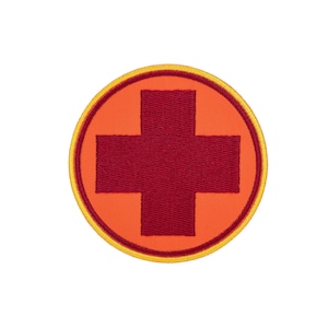 May include: A circular embroidered patch featuring a dark red cross centered on a bright orange background. The patch is finished with a thin dark red inner border and a vibrant yellow outer stitched edge, creating a clean and defined circular shape.