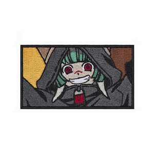 May include: A rectangular embroidered patch featuring a character with green hair and red eyes wearing a dark gray hooded cloak. The character has a wide grin and a small red tag hanging from the hood. The background includes yellow and brown sections.