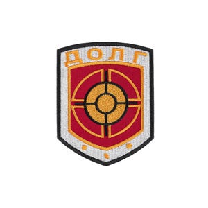 May include: A shield-shaped embroidered patch with a black border. The center features a red shield with a yellow crosshair target symbol. Above the target, the Cyrillic text "ДОЛГ" is stitched in yellow. The background is white with three yellow dots.