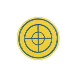 Può includere: Una toppa ricamata circolare con uno sfondo giallo brillante e un design a mirino blu centrato al centro. La toppa presenta un bordo giallo spesso e un contorno blu cucito, creando una grafica a forma di bersaglio su base in tessuto.