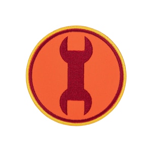 Op de afbeelding: Een ronde geborduurde patch met een feloranje achtergrond en een donkerrood silhouet van een steeksleutel in het midden. De patch is afgewerkt met een donkerrode binnenrand en een felgele buitenrand met stiksel.