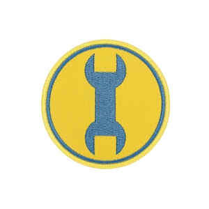 May include: A circular embroidered patch featuring a bright yellow background with a blue border. Centered on the patch is a blue double-ended wrench icon. The embroidery has a visible texture throughout the design, creating a clean and defined graphic appearance.