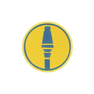 Op de afbeelding: Een ronde geborduurde patch met een felgele achtergrond en een blauwe rand. In het midden van de patch staat een blauwe afbeelding van een raketgranaat, weergegeven met een puntige kop en een gesegmenteerd lichaam.