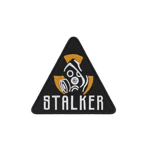 May include: A triangular black embroidered patch featuring a white gas mask graphic centered over a yellow radiation symbol. The word STALKER is stitched in white capital letters at the bottom of the patch, which has a black stitched border.