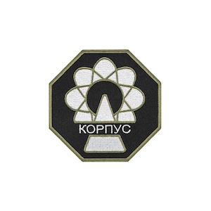 May include: An octagonal embroidered patch with a black background and an olive green border. The design features a white stylized circular emblem with a central triangle and the Cyrillic text KOPПУC embroidered in white below the emblem.