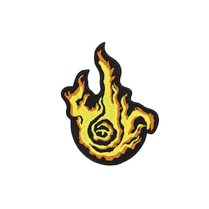 May include: An embroidered patch featuring a stylized flame design with a central spiral element. The flame is rendered in vibrant yellow and orange thread, outlined with a thick black border that defines the irregular, flickering shape.