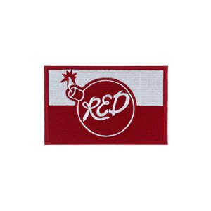 Puede incluir: Un parche rectangular bordado con un diseño dividido horizontalmente, con la mitad superior blanca y la mitad inferior roja. En el centro, un contorno circular blanco contiene la palabra RED en letra estilizada y un icono de bomba.