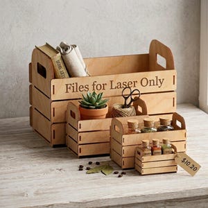 Puede incluir: Un conjunto de cuatro cajas de madera de color claro encajables con asas recortadas. La caja más grande presenta el texto grabado "Files for Laser Only". Las cajas contienen una pequeña suculenta, unas tijeras y varios frascos de especias.