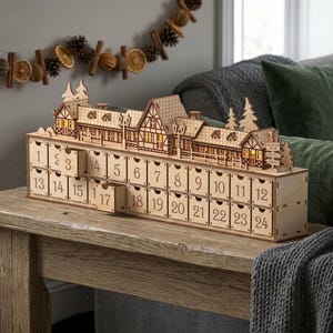 Puede incluir: Un calendario de adviento de madera con una escena de pueblo de dos pisos con ventanas iluminadas sobre una base de veinticuatro cajones numerados. La estructura incluye pinos recortados y una señal con las palabras North Pole, Santa y Gifts, cajones 3 y 17 abiertos.