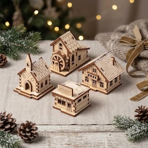 May include: A set of four miniature wooden buildings including a church with a steeple, a water mill with a wheel, a shop with the word SHOP on the front, and a house with a balcony. Each structure features light brown wood and roof details.