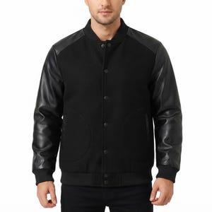 Può includere: Una giacca stile varsity nera con corpo in misto lana e maniche in ecopelle nera a contrasto. La giacca presenta colletto, polsini e orlo a coste, chiusura frontale con bottoni a pressione e due ampie tasche anteriori arrotondate.