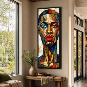 May include: A vertical rectangular wall art piece featuring a stylized portrait of a person composed of geometric, stained-glass-like segments in vibrant shades of blue, red, yellow, and brown, framed in a thin black border on a neutral wall.