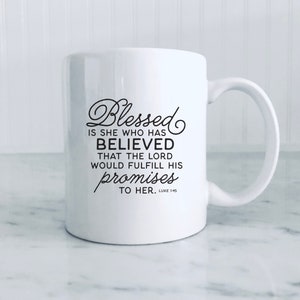 May include: White ceramic mug with a curved handle. The mug features black script that reads "Blessed is she who has believed that the Lord would fulfill his promises to her. Luke 1:45."