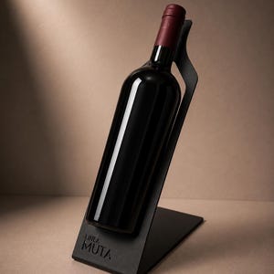 Op de afbeelding: Een donkere glazen wijnfles met een bordeauxrode dop, rustend in een hoek op een matzwarte metalen standaard. De voet van de standaard bevat de tekst "LINEA MUTA" in een strak, schreefloos lettertype. Het ontwerp houdt de fles schuin.
