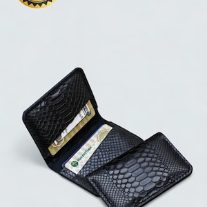 May include: A black bifold wallet featuring a textured snakeskin pattern. The wallet is open, revealing multiple interior card slots containing two credit cards. The exterior surface has a glossy finish with a distinct scale-like appearance.
