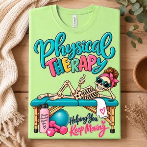 Op de afbeelding: Een lichtgroen t-shirt met een afbeelding van een skelet dat op een fysiotherapietafel ligt, met een zonnebril en een roze hoofdband. De tekst luidt Physical Therapy en Helping You Keep Moving, met illustraties van een waterfles en dumbbells.