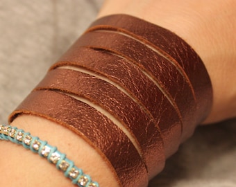 Könnte beinhalten: Ein braunes Lederarmband mit einem türkisfarbenen und silbernen Strass-Armband am Handgelenk einer Person.