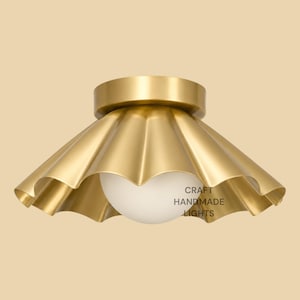 May include: A brass flush mount ceiling light featuring a wide, scalloped metal shade with a brushed gold finish and a central white spherical glass globe. The text CRAFT HANDMADE LIGHTS is printed in black on the surface of the glass globe.