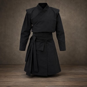 May include: A solid black wrap-style jacket and skirt set featuring a structured crossover bodice with long sleeves and shoulder detailing. The skirt includes a wide waistband with long, hanging fabric ties and a small rectangular pocket flap.