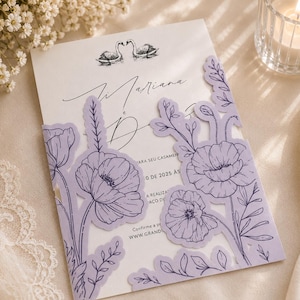 Pode incluir: Um convite de casamento branco com uma ilustração a tinta preta de dois cisnes no topo. O cartão está dentro de uma capa de papel cortada a laser em tom lilás, decorada com desenhos de papoulas e folhagens nos painéis frontais.