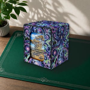 May include: A square deck box featuring a vibrant purple, blue, and black cosmic octopus design with swirling tentacles and planetary motifs. A rectangular cutout on the front displays a trading card showing a tree in a landscape.