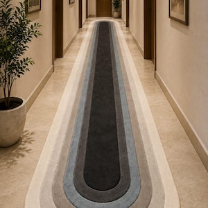 Puede incluir: Una alfombra de pasillo larga y estrecha que presenta una serie de bandas concéntricas de forma rectangular redondeada en un degradado de colores. La paleta transita desde un centro negro carbón profundo hacia azul pizarra, gris y beige.