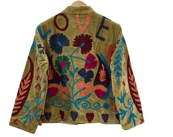 May include: An olive green velvet jacket featuring colorful floral embroidery and the word LOVE stitched across the upper back. The design includes paisley motifs, heart shapes, and intricate leaf patterns in shades of blue, red, and orange.