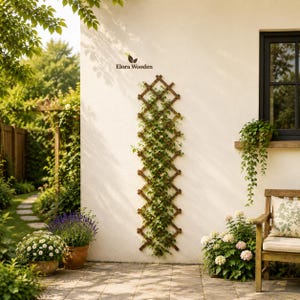 Puede incluir: Un enrejado de madera marrón de forma alta montado en una pared exterior blanca, con un patrón de rejilla en forma de diamante. El enrejado está parcialmente cubierto con enredaderas verdes. El texto Elora Wooden está impreso arriba.