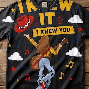 May include: A black t-shirt featuring a graphic of a person with long brown hair wearing a yellow plaid shirt and cow-print bell-bottom trousers, playing an acoustic guitar. The text reads I KNEW IT and I KNEW YOU, with a red cowboy hat, clouds, and stars.