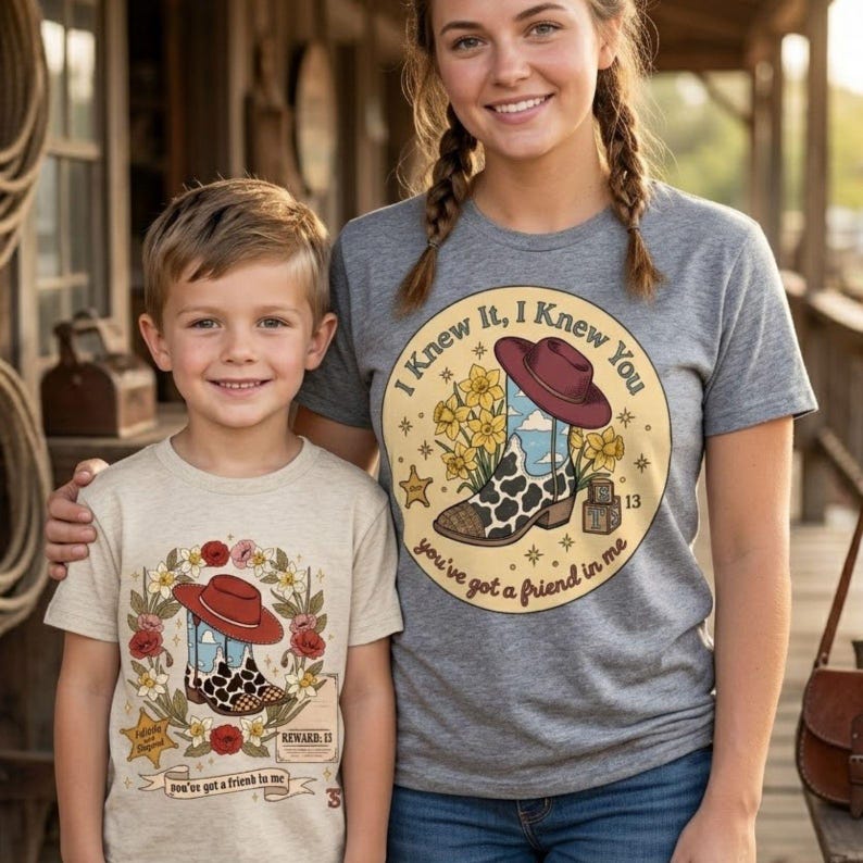 May include: A heather gray t-shirt with a graphic of a cowboy boot, a hat, and yellow flowers, featuring the text "I Knew It, I Knew You" and "you've got a friend in me," alongside a beige t-shirt with a similar boot graphic and floral border.