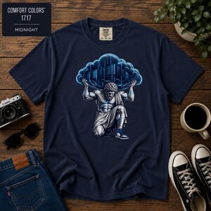 May include: A midnight blue t-shirt featuring a graphic of a muscular figure kneeling and holding up a large, glowing blue cloud containing a city skyline. The shirt label reads Comfort Colors 1717. The design includes binary code patterns.