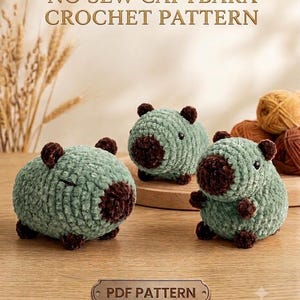 May include: Three plush capybara figures made of sage green and dark brown yarn. The text NO SEW CAPYBARA CROCHET PATTERN is at the top, and a label reading PDF PATTERN is at the bottom. The figures have small dark eyes and rounded ears.