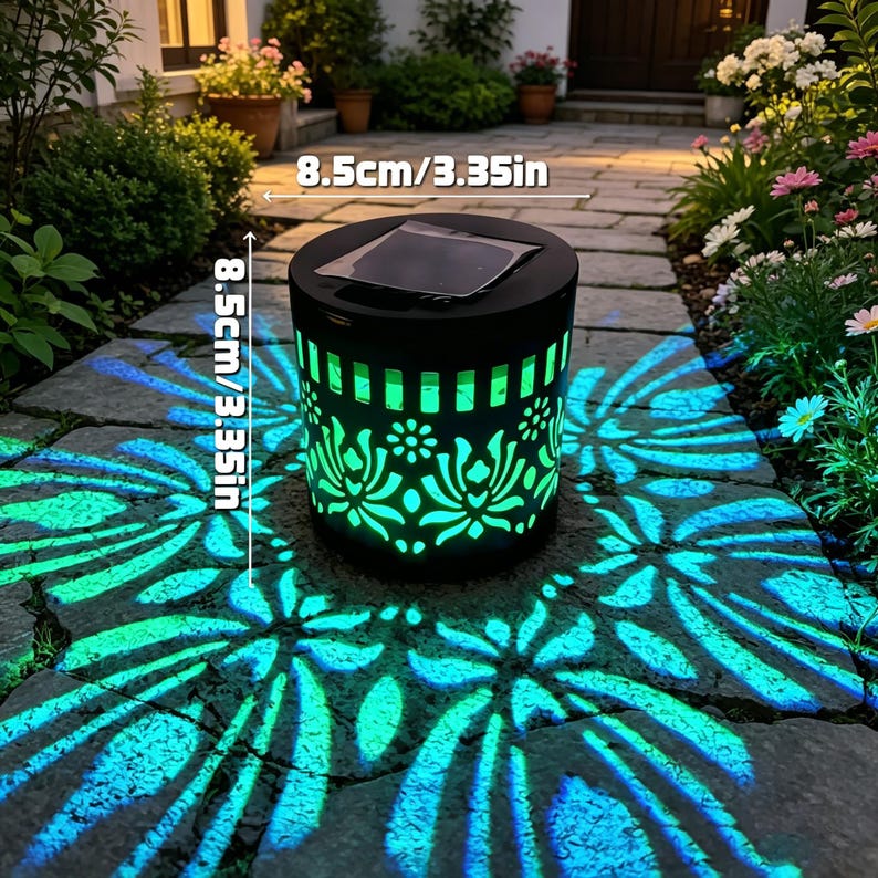 May include: A cylindrical black solar garden light with a cutout floral pattern that projects a bright turquoise light onto the ground. The device features a square solar panel on top and measures 3.35 inches in height and 3.35 inches in diameter.