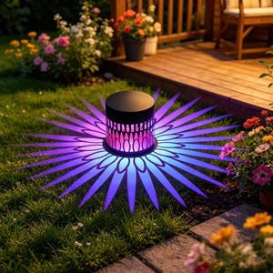 May include: A cylindrical black solar garden light sits on the grass, casting a vibrant purple and blue starburst pattern of light onto the ground. The light features a cut-out design that projects long, pointed rays across the lawn surface.
