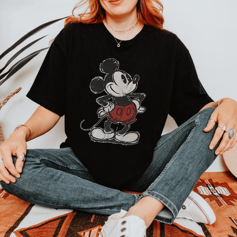 May include: A black short-sleeve t-shirt featuring a distressed graphic print of Mickey Mouse. The character is depicted in black, white, and red with a vintage-style texture. The shirt has a crew neckline and a relaxed fit.