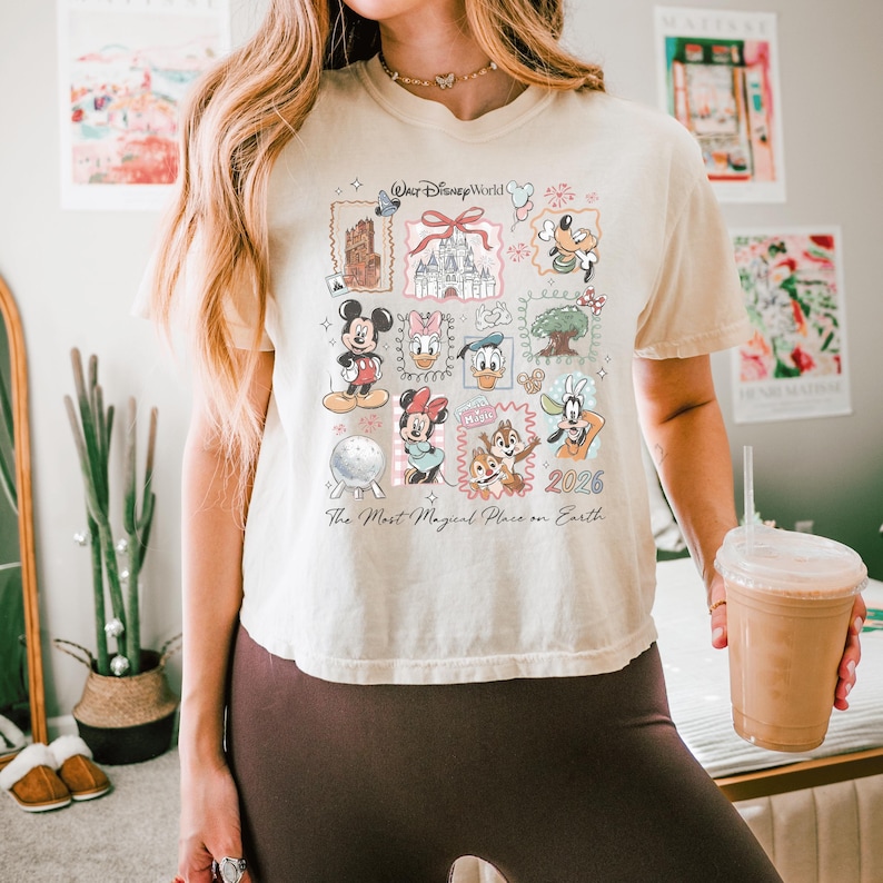 K&ouml;nnte beinhalten: Ein cremefarbenes Kurzarm-T-Shirt mit einem Grafikdruck von Walt Disney World-Symbolen und Charakteren wie Mickey Maus, Minnie Maus, Donald Duck und Goofy sowie dem Text "Walt Disney World" und "The Most Magical Place on Earth".