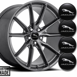 Pode incluir: Uma jante de liga leve cinzento-escura de múltiplos raios com uma tampa central com o logótipo Jaguar. À direita, são apresentadas quatro tampas centrais pretas circulares adicionais, cada uma com o emblema do jaguar saltador e o texto JAGUAR.