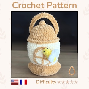 Può includere: Uno schema all'uncinetto che raffigura un oggetto di peluche a forma di lanterna color marrone chiaro e bianco con un manico. Una piccola ape gialla e bianca è attaccata sul davanti. Il testo 'Crochet Pattern' e 'Difficulty' con stelle sono visibili.