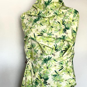 May include: A white fabric with a green floral print. The fabric is draped over a dress form.