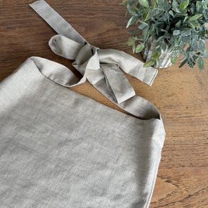 May include: A light gray linen tote bag with a long strap that ties at the top. The strap is made of the same linen fabric as the bag.