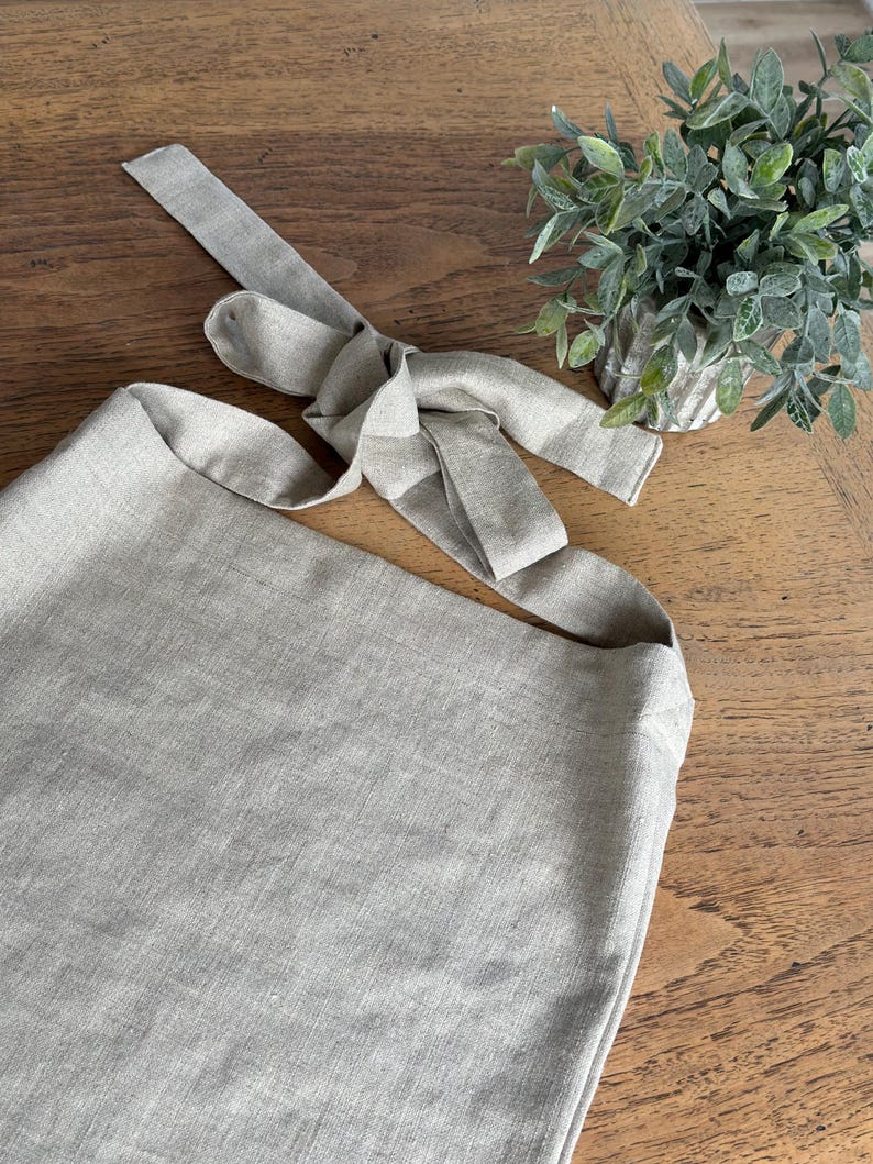 May include: A light gray linen tote bag with a long strap that ties at the top. The strap is made of the same linen fabric as the bag.