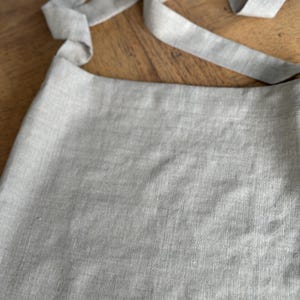 May include: A light gray linen tote bag with a long strap that can be tied into a bow.
