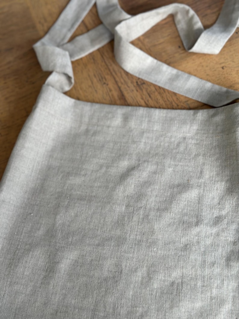 May include: A light gray linen tote bag with a long strap that can be tied into a bow.